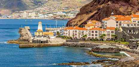 En kust med byggnader som har röda tak, en hamn och kullar i bakgrunden. (AI-genererad text)