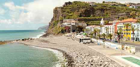 En strand med sten vid foten av en klippa med byggnader och terrasserade fält. (AI-genererad text)