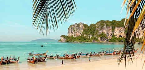 En strand med longtailbåtar och klippor vid havet. (AI-genererad text)