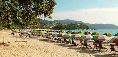 En strand med rader av färgglada parasoller och solstolar. (AI-genererad text)