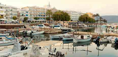 Småbåtar förtöjda vid en hamn, med byggnader och palmer i bakgrunden. (AI-genererad text)