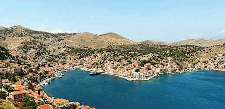 Bild på en bukt omgiven av kullar med hus och småbåtar vid vattnet. (AI-genererad text)