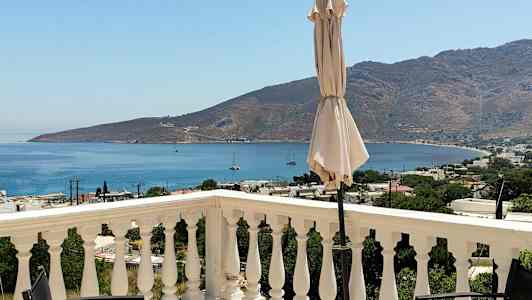 En vy från en terrass med räcken, en parasoll och en utsikt över havet och berg i bakgrunden. (AI-genererad text)