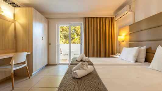 Ett hotellrum med två enkelsängar, skrivbord, och en glasdörr som leder till en balkong. (AI-genererad text)