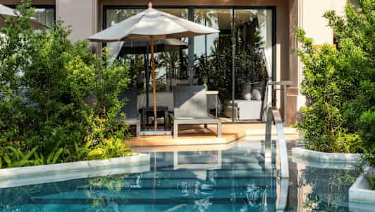 En terrass med solstolar och parasoll vid en pool, omgiven av grönska. (AI-genererad text)