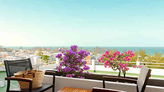 En balkong med bord och stolar, blommor och havsutsikt. (AI-genererad text)