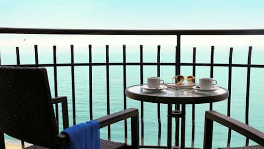 Balkong med bord och stolar som vetter mot havet. (AI-genererad text)