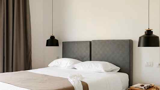 Hotellrum med grå sänggavel, vit bädd och två svarta hängande lampor. (AI-genererad text)