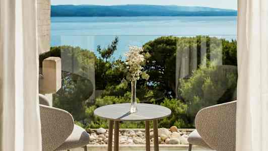 En borddekoration med blommor vid ett bord framför fönster med utsikt över havet och grönska. (AI-genererad text)