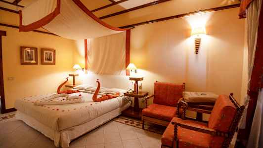 Ett hotellrum med en stor säng dekorerad med handdukar formade som svanar och blommor, två stolar och ett bord. (AI-genererad text)