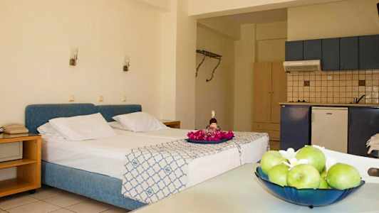 Rummet har en säng med blått sänggaveltäcke, ett kök och ett bord med frukt. (AI-genererad text)