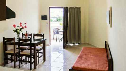 Ett rum med ett matbord och stolar, en bäddsoffa, och en öppning som leder till en balkong. (AI-genererad text)