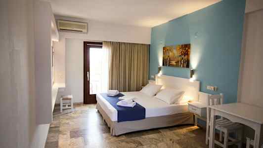 Ett hotellrum med en dubbelsäng, blå väggdekoration och ett bord med stolar. (AI-genererad text)