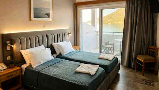 Hotellrum med två enkelsängar, sängbord och tavla på väggen. Balkong med utsikt över vatten och berg. (AI-genererad text)