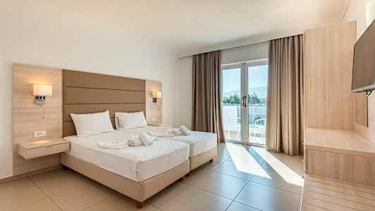 Ett ljust hotellrum med två sängar, en balkongdörr med utsikt och möbler av trä. (AI-genererad text)