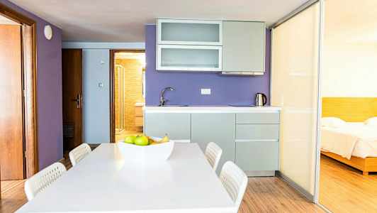 Ett kök med lila väggar, en matplats och en skjutdörr som leder till ett sovrum. (AI-genererad text)