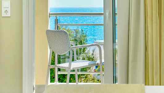 Utsikt från ett rum mot en balkong med en stol och havet i bakgrunden. (AI-genererad text)