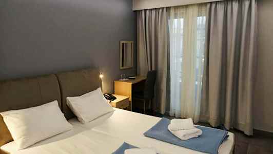 Ett hotellrum med en dubbelsäng, skrivbord och ett fönster med gardiner. (AI-genererad text)