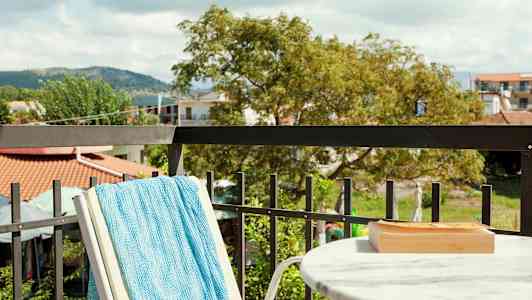 Utsikt från en balkong med ett marmorbord, en turkos handduk på en stol och grönska i bakgrunden. (AI-genererad text)