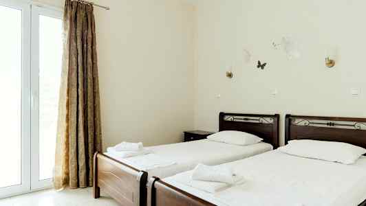 Två enkelsängar med vita sängkläder och mörka träsänggavlar, belägna i ett ljust rum med gardiner och väggdekorationer. (AI-genererad text)