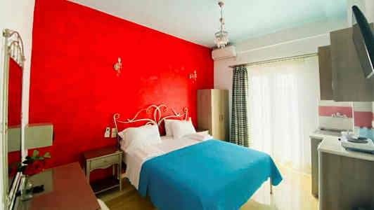 Ett hotellrum med en dubbelsäng, rött väggparti, och ljusblå överkast. (AI-genererad text)