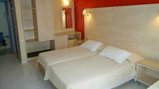 Ett hotellrum med två enkelsängar bredvid varandra, en garderob och ett bord med spegel. (AI-genererad text)