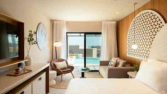 Ett elegant hotellrum med moderna möbler, en soffa, en fåtölj, ett sängområde med prydnadshuvudgavel, en stor spegel och glasdörrar som öppnar mot en swimmingpool utomhus. (AI-genererad text)