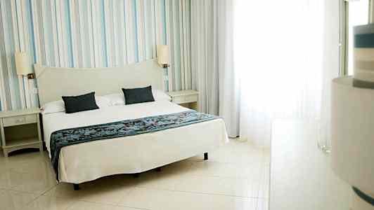 Ett hotellrum med en stor säng täckt med vita sängkläder och två mörkblå kuddar. (AI-genererad text)