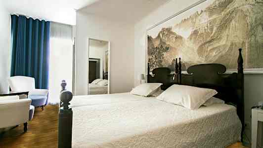 Säng med utsnidad huvudgavel i ett rum med en väggspegel och sittmöbler. (AI-genererad text)