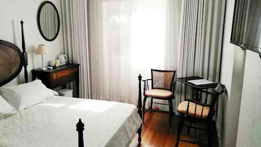 Ett hotellrum med en säng, skrivbord och stol, samt ett fönster med vita gardiner. (AI-genererad text)