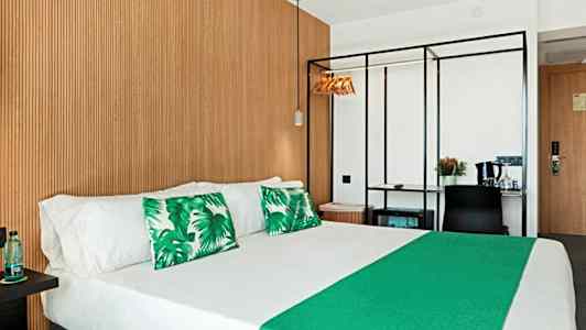 Hotellrum med dubbelsäng, gröna dekorationskuddar och träpanel på väggen. (AI-genererad text)