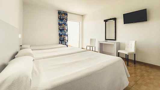 Ett hotellrum med tre enkelsängar, ett skrivbord med spegel, två stolar och en väggmonterad TV. (AI-genererad text)