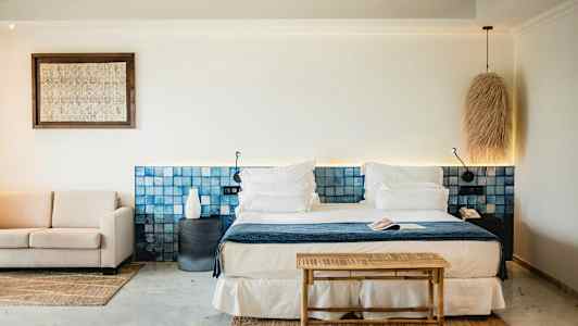 Ett stilrent hotellrum med en dubbelsäng, blå sänggavel, soffgrupp och ljusa dekorativa element. (AI-genererad text)