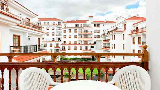 Utsikt från en balkong mot en byggnad med vita fasader och röda tak. (AI-genererad text)