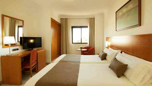 Ett hotellrum med två sängar, ett skrivbord med en stol och en TV, samt ett fönster och en fåtölj. (AI-genererad text)