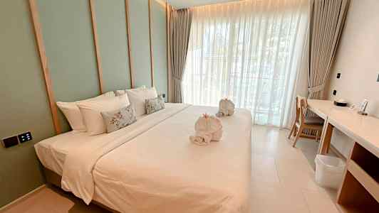 Bild av ett modernt hotellrum med en stor bäddad säng, vita sängkläder och dekorativa kuddar, samt handdukar formade som svanar. Rummet har fönster med ljusa gardiner och en skrivbordsplats vid sidan av. (AI-genererad text)