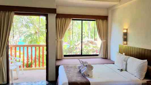 Ett hotellrum med öppen dörr till en balkong och en säng med dekorationer. (AI-genererad text)