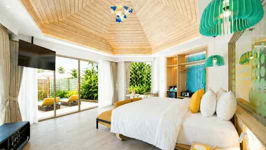 Ett ljust och rymligt hotellrum med modern inredning, en stor säng och stora fönster som vetter mot en uteplats med solstolar och grönska. (AI-genererad text)