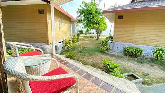 Två stolar med röda dynor på en veranda med utsikt över trädgård och hav. (AI-genererad text)