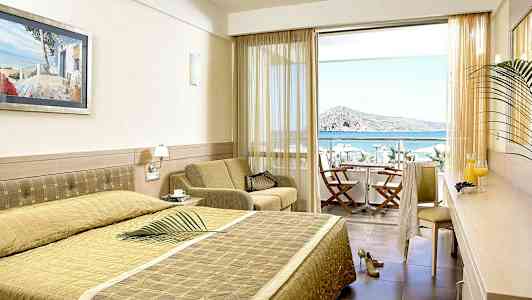 Ett hotellrum med en stor säng, sittgrupp och balkong med utsikt över havet. (AI-genererad text)