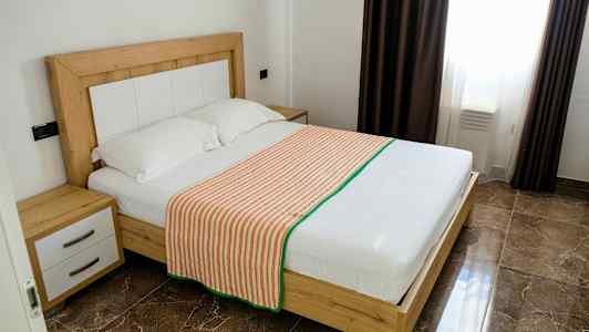 Ett sovrum med en dubbelsäng med trästomme, två kuddar och ett randigt överkast. (AI-genererad text)