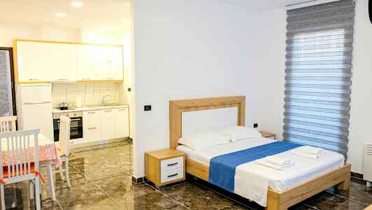 Ett sovrum med en dubbelsäng, bord med stolar samt en liten köksdel. (AI-genererad text)