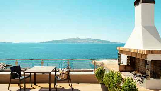 En terrass med bord, stolar och grill med utsikt över havet och en avlägsen ö. (AI-genererad text)