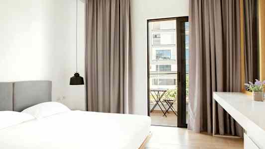 Ett modernt sovrum med en stor säng, grå gardiner och en dörr som leder till en balkong utanför. (AI-genererad text)