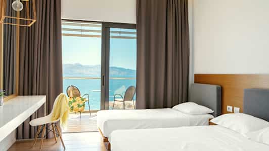 Hotellrum med två enkelsängar och utgång till en balkong med utsikt över havet. (AI-genererad text)