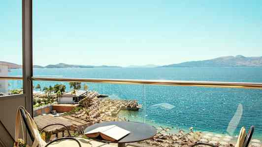 Utsikt från en balkong mot en strand och hav med parasoller och solstolar. (AI-genererad text)