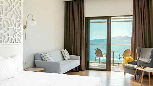 Hotellrum med säng, soffa, fåtölj och balkong med havsutsikt. (AI-genererad text)