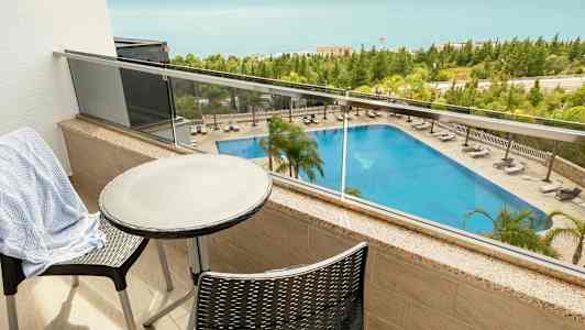 Vy från en balkong med bord och stolar som visar en pool och havet i bakgrunden. (AI-genererad text)