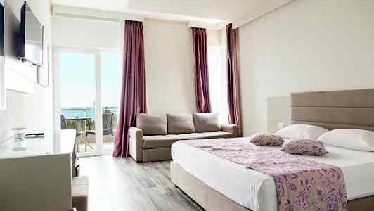 Ett hotellrum med en dubbelsäng, en soffa och en balkong med utsikt mot havet. (AI-genererad text)