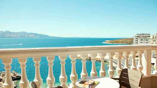 Utsikt från en balkong med en vit räcke över havet, ett bord och en stol. (AI-genererad text)